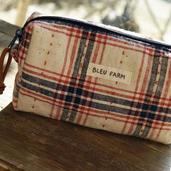 a small zipper pouch in cream colour fabric with red and black pattern on a wooden surface, the fabric looks vintage and