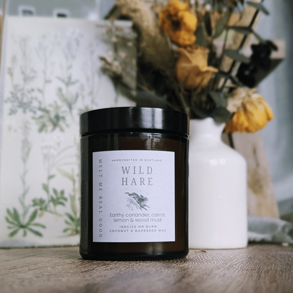A brown jar containing a candle named The Hare with dried flowers in the background