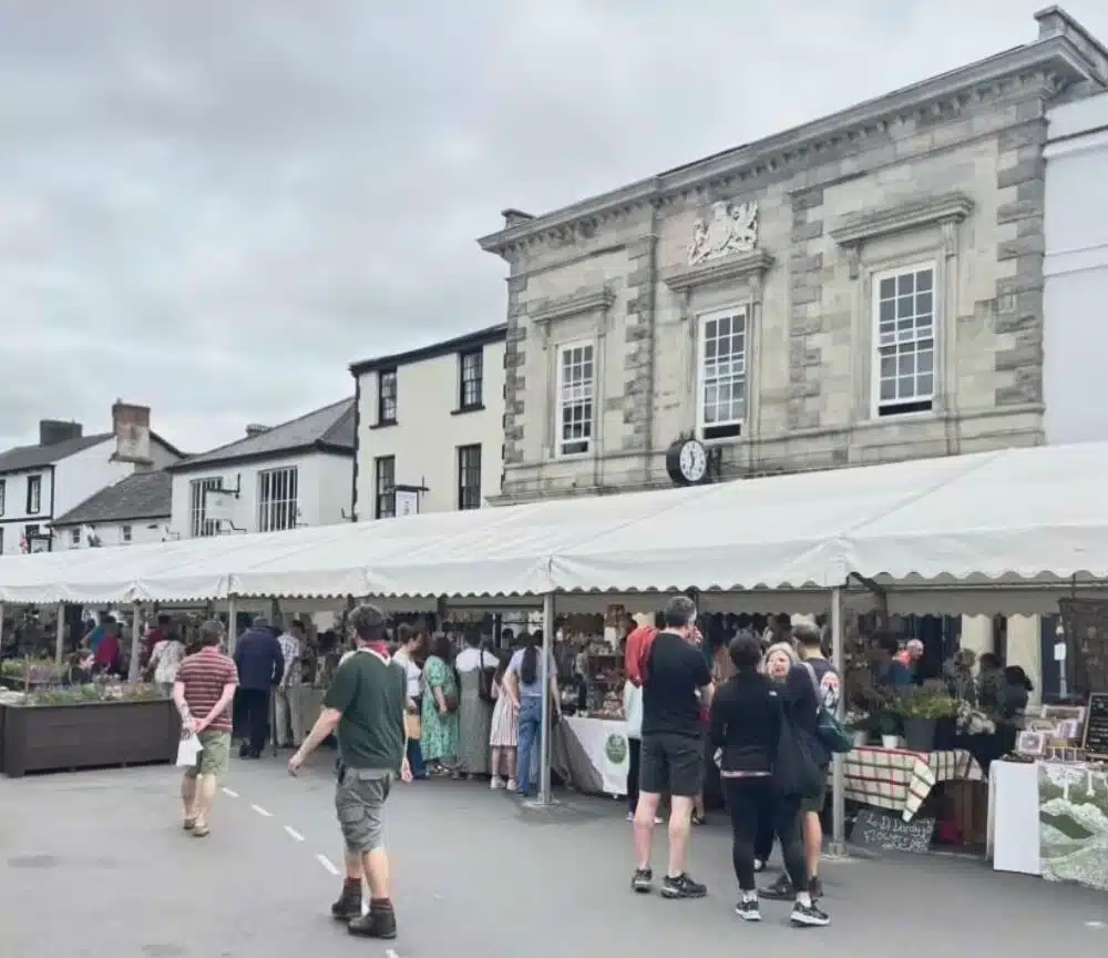 the image shows a large marquee in the high street, with artists selling their wares, with a large group of visitors. behnind th emarquee are the high street buildings