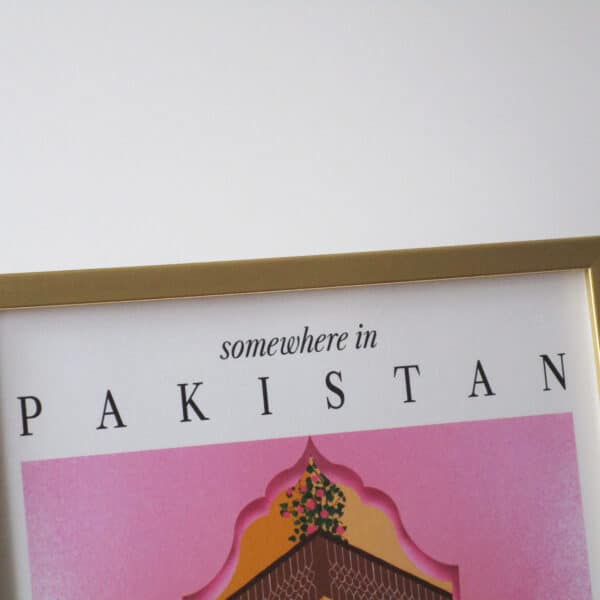 A close-up shot of a gold metallic frame with a colourful print with text 'somewhere in Pakistan' showing the top of an illustration of a pink Mughal arch and a haveli (mansion courtyard).