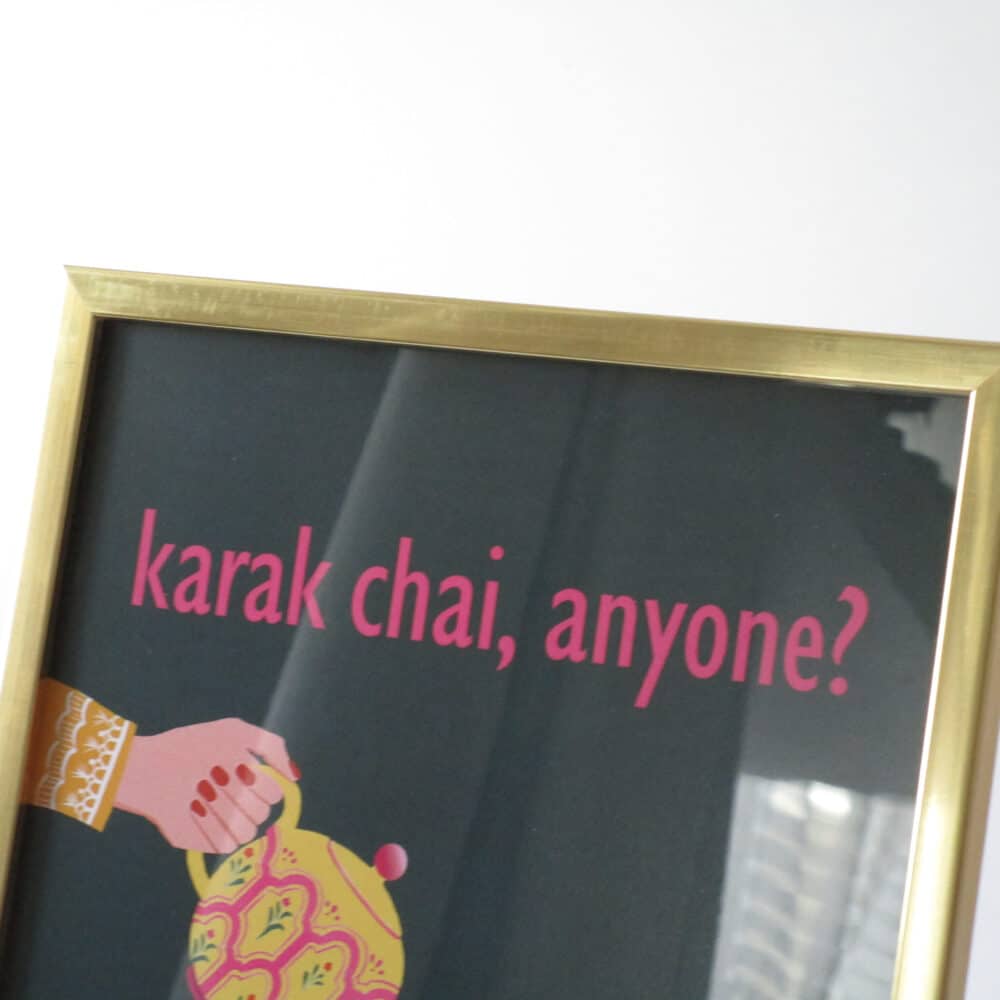 A close-up shot of a gold metallic frame with a dark green and pink print inside that reads 'karak chai, anyone?' and a hand is pouring tea out of a desi teapot.