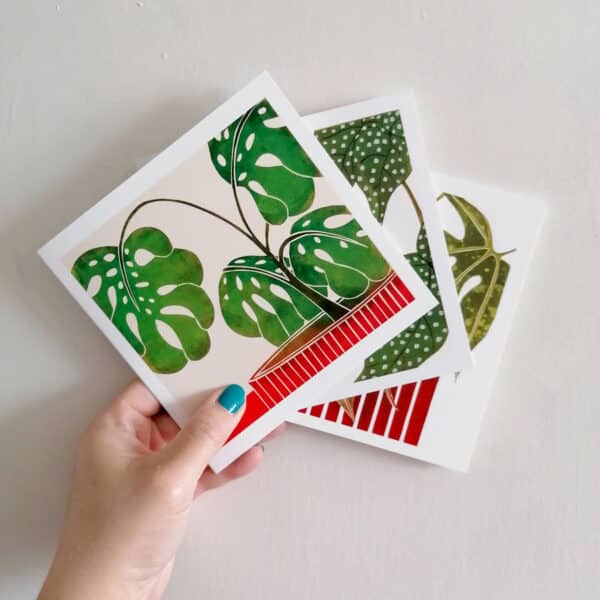 my hand holding 3 of my botanical greeting cards. Top card is of a Swiss cheese plant