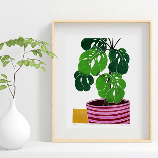 colourful Swiss cheese plant lino print in a wooden frame next to a real plant