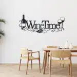 Black metal wall art featuring the words “Wine Time” with a wine bottle replacing the letter “I,” two wine glasses, grapevine accents, and grape clusters, displayed above a light wood dining table in a bright, modern dining room or kitchen.