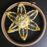 A large yellow and white flower in a round embroidery hoop on a black background