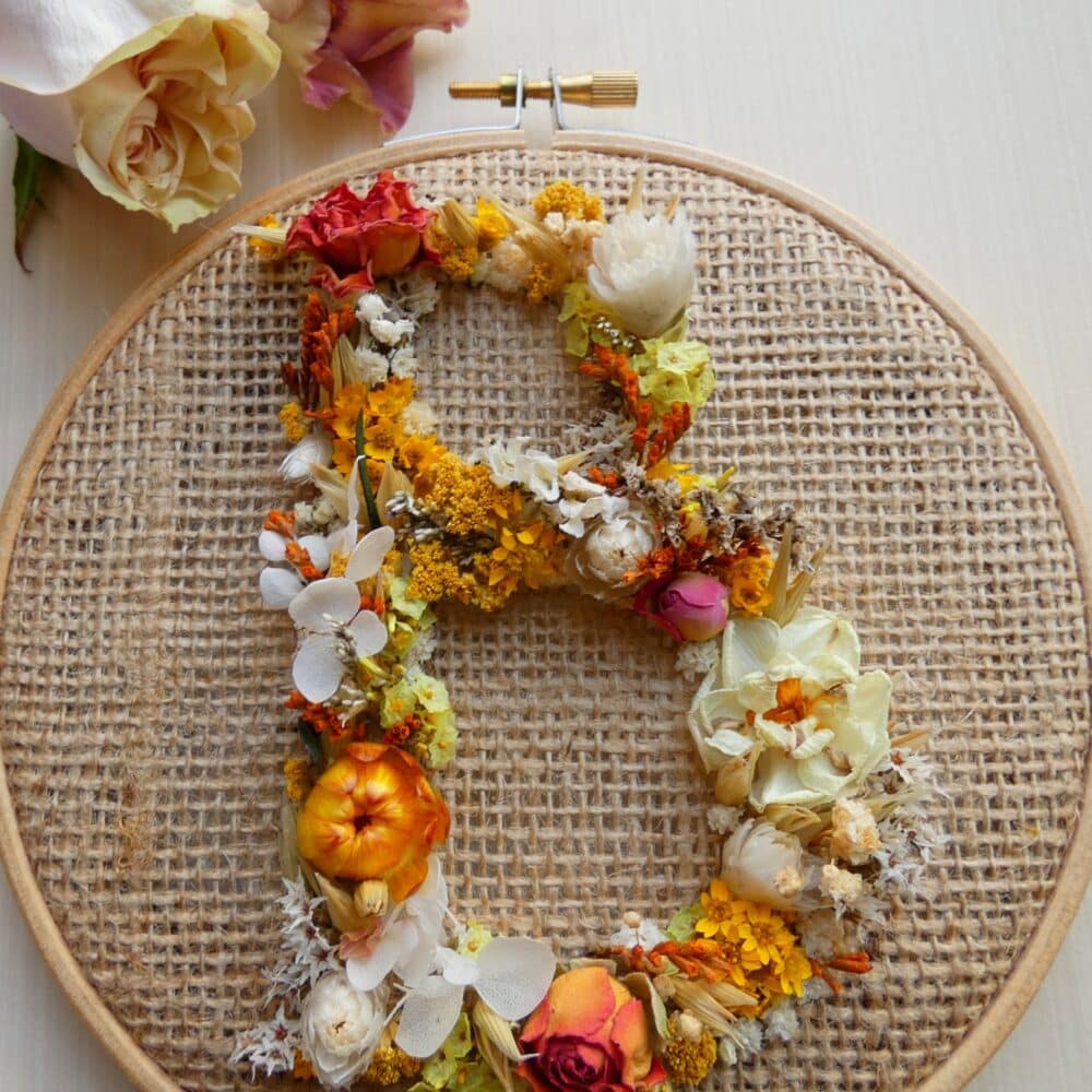 A round hoop showing a letter B made of orange and white dried flowers on a hessian background - dried flower art
