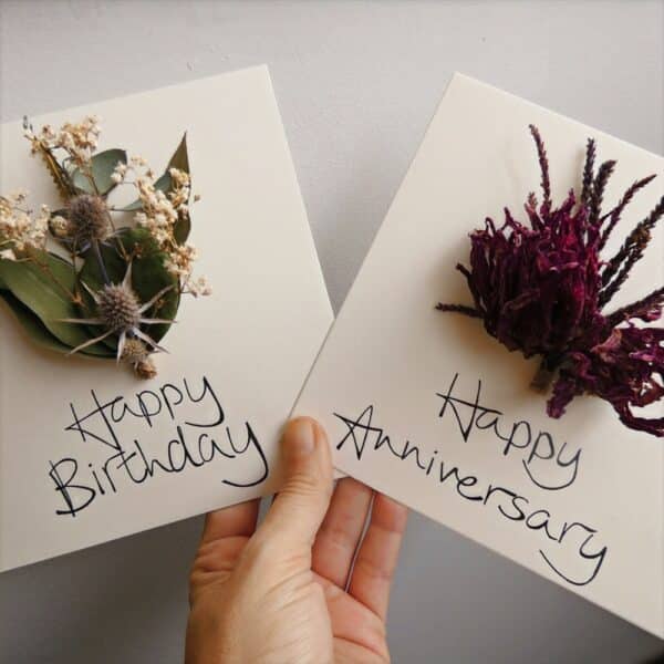 Two hand penned greetings cards with dried flower bouquets attached to each card