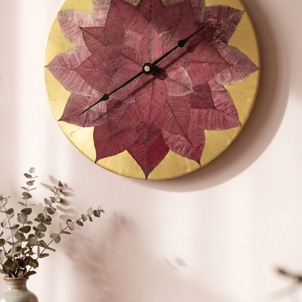 A round clock is hung on a pale pink wall, each hour mark is indicated by the tip of a poinsettia bract on a gold background - dried flower art