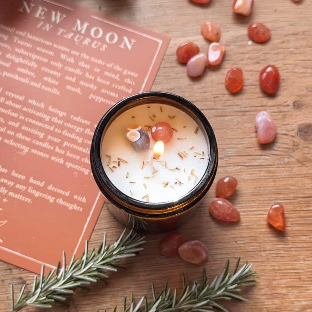Image shows a lit candle topped with carnelian crystals and rosemary.