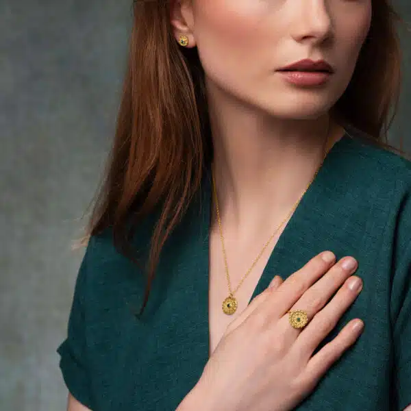 A model in a green dress wears a ring, earrings and pendant from the Odeda Jewellery mandala collection, intricately detailed organic discs in 18ct gold vermeil studed with gemstones.