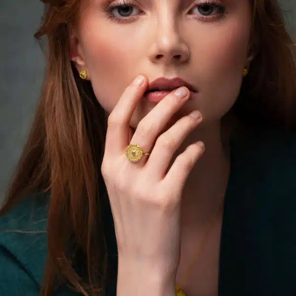 A model in a green dress stares at us from the camera with her hand to her face. On her hand is a gorgeous intricately detailed mandala ring from Odeda Jewellery featuring a delicate green emerald.