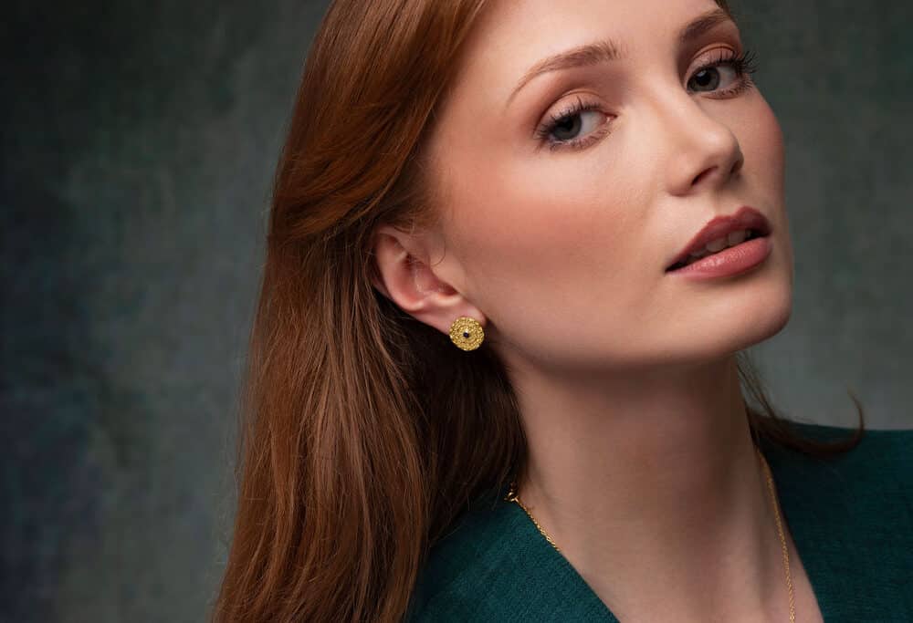 A model in a green dress looks at the camera with a gorgeous 18ct gold mandala earring from Odeda Jewellery featuring a beautiful sapphire