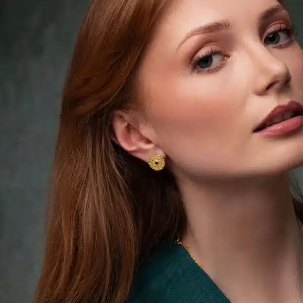 A model in a green dress looks at the camera with a gorgeous 18ct gold mandala earring from Odeda Jewellery featuring a beautiful sapphire