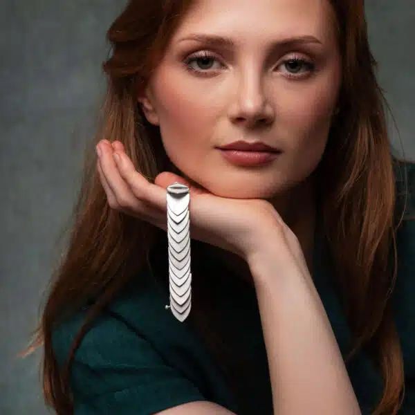 A model looks at the camera with a gorgeous bracelet consisting of 29 arch shaped pieces of thick silver hinged together dangling from her hand.