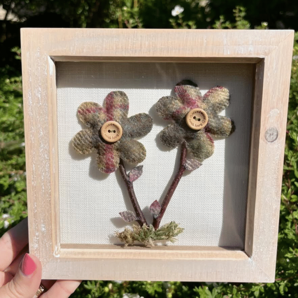 A rustic piece of framed artwork featuring two tartan flowers, twigs and dried leaves