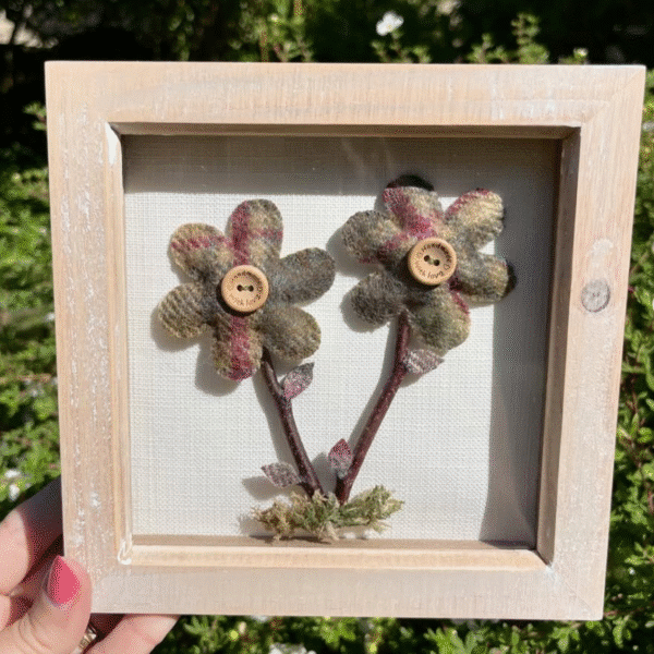 A rustic piece of framed artwork featuring two tartan flowers, twigs and dried leaves