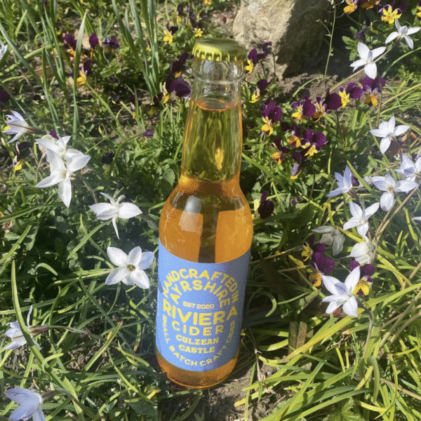 A glass bottle of cider standing amongst flowers