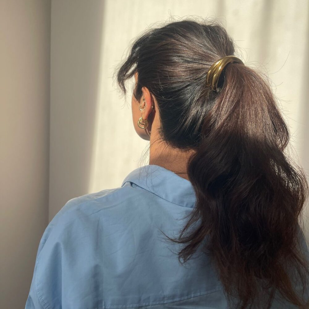 girl with brunette hair with a gold ponytail hair accessory in her hair. wearing blue shirt