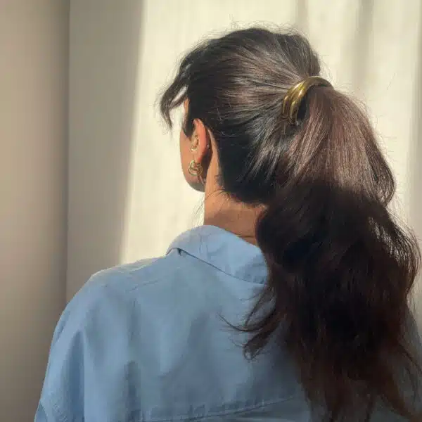 girl with brunette hair with a gold ponytail hair accessory in her hair. wearing blue shirt