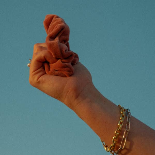 Model holding burnt orange velvet scrunchie to the sky