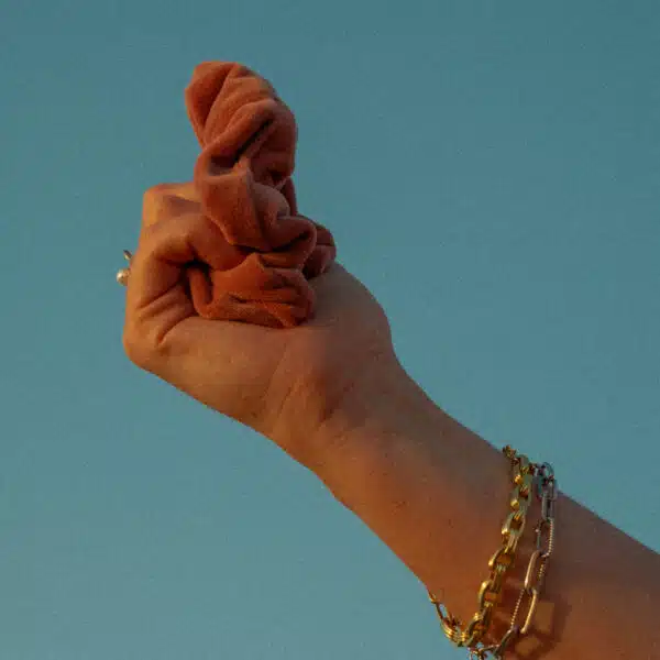 Model holding burnt orange velvet scrunchie to the sky