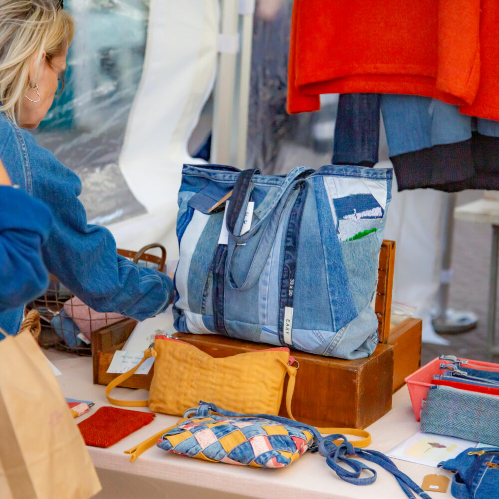 People browsing a market stall of upcycled denim bags
