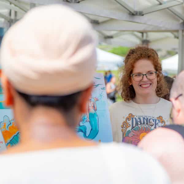 A smiling woman on a market stall with bright prints and customers