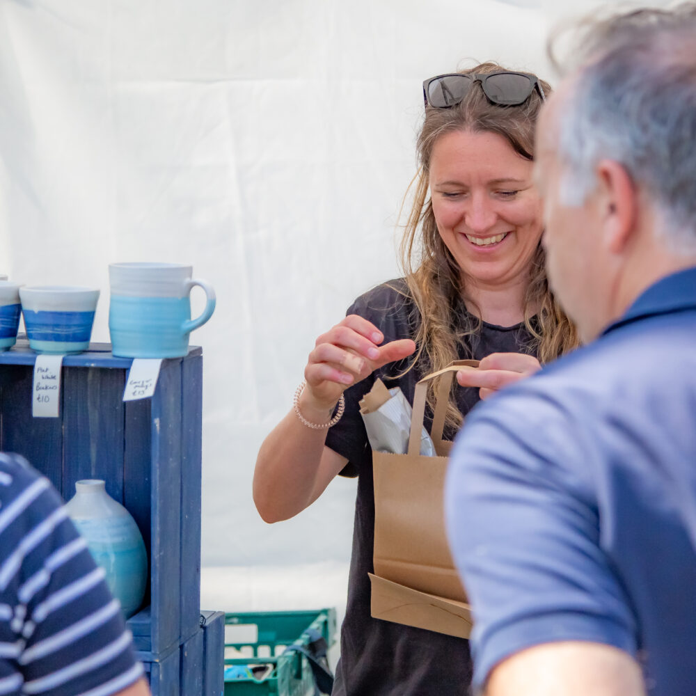 A female market trader passing a bag of ceramics to a customer