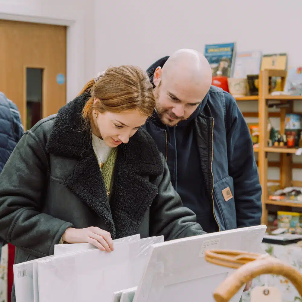 Two customers looking through vintage artwork at a So Retro vintage fair