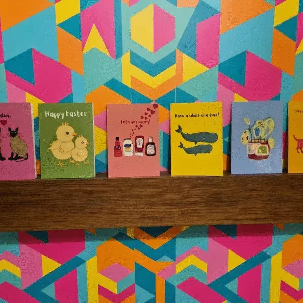 A wooden mantle piece with 6 brightly coloured greetings cards of different designs.