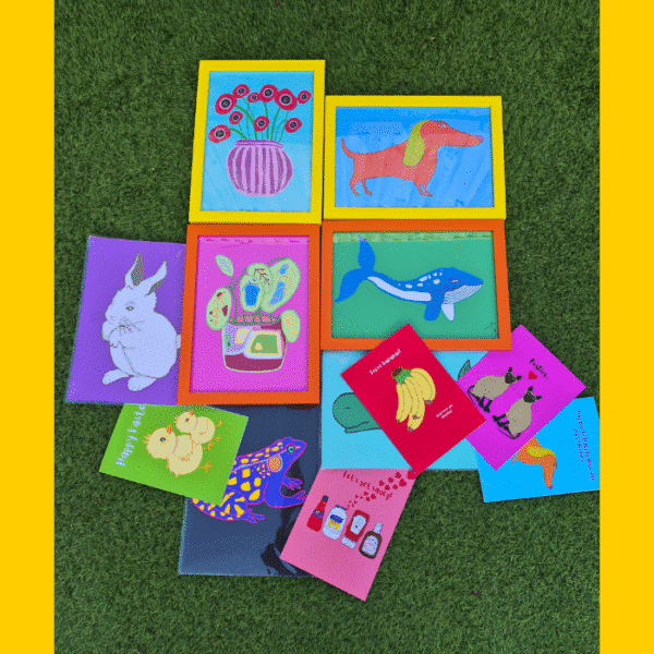 A selection of brightly coloured prints and greetings cards on grass. Juicy Prints