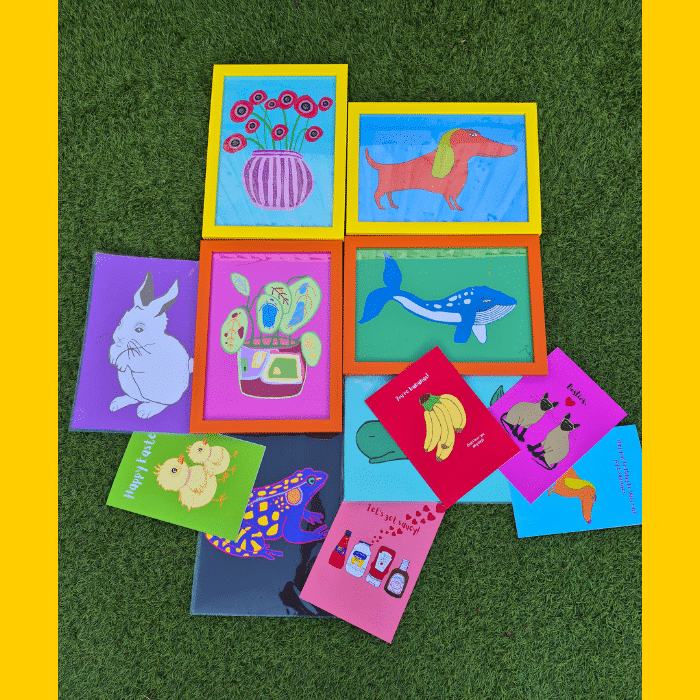 A selection of brightly coloured prints and greetings cards on grass. Juicy Prints