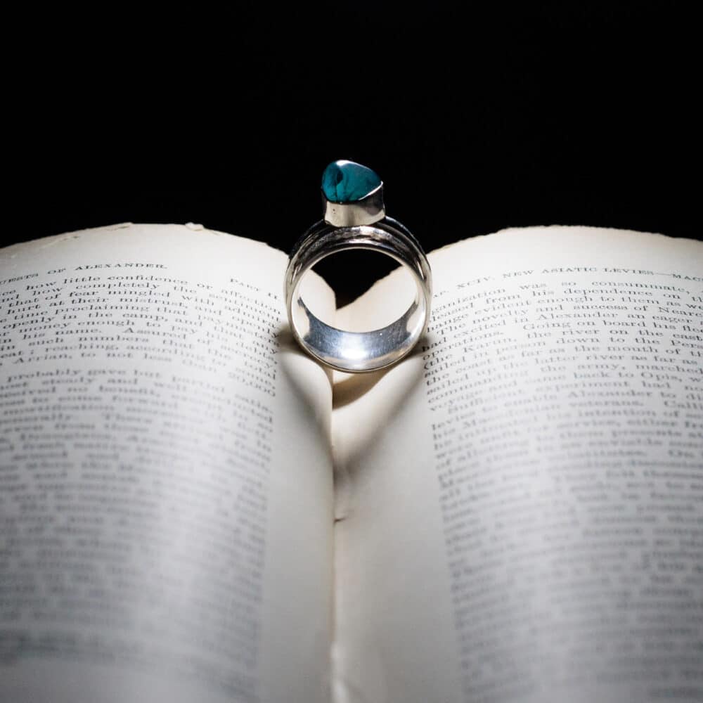 Purple Phoenix Jewellery-Silver and green coloured gem set stone on a book, lit so it shows a heart shadow in the centre of the book