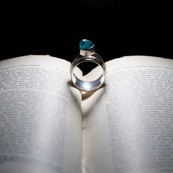 Purple Phoenix Jewellery-Silver and green coloured gem set stone on a book, lit so it shows a heart shadow in the centre of the book