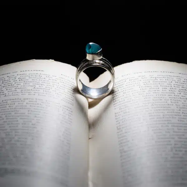 Purple Phoenix Jewellery-Silver and green coloured gem set stone on a book, lit so it shows a heart shadow in the centre of the book