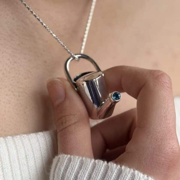 Purple Phoenix Jewellery-Silver watering can with blue topaz set in the spout, being held by a hand whilst being worn.