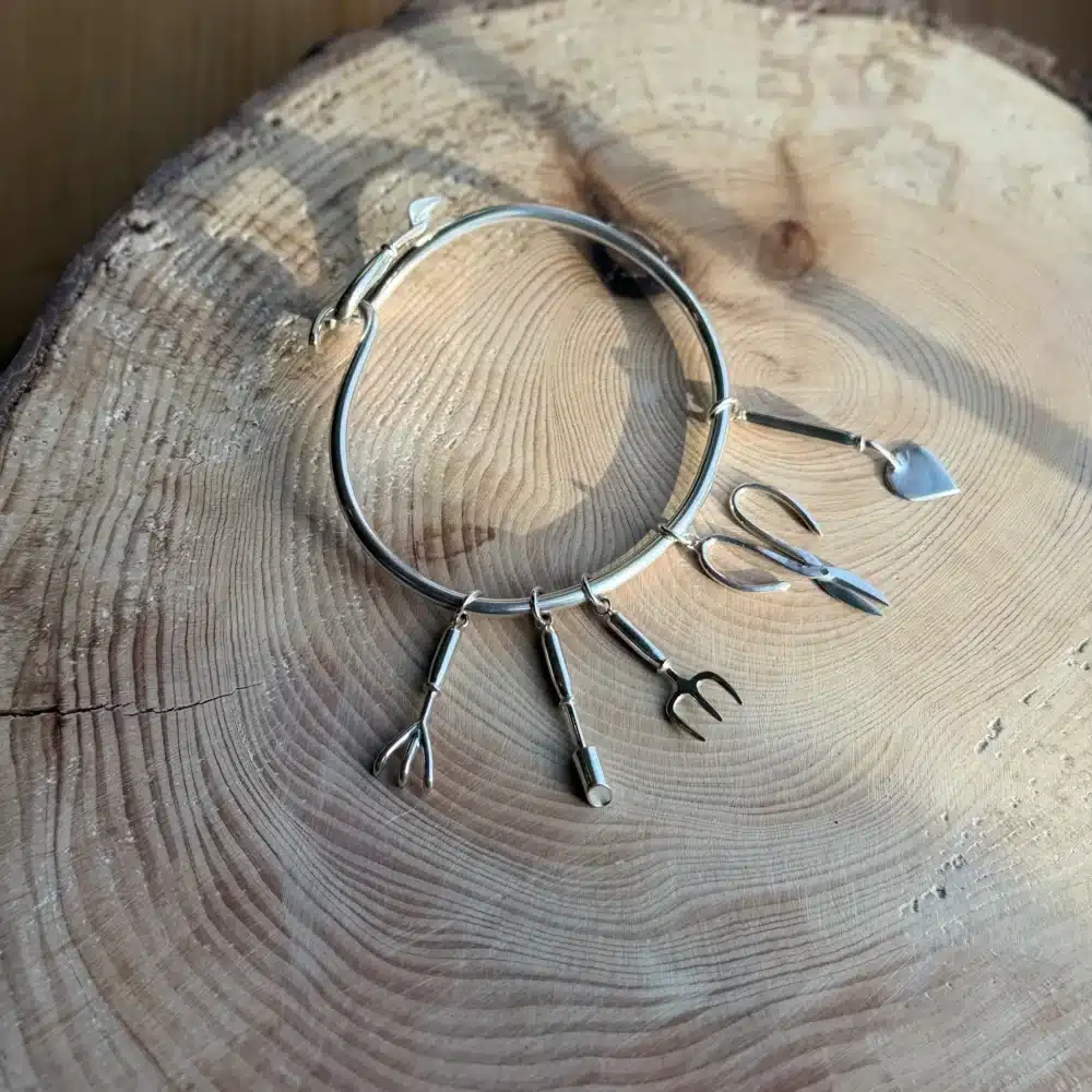 Purple Phoenix Jewellery-Silver trowel bangle with various charms of gardening tools, on a wooden background