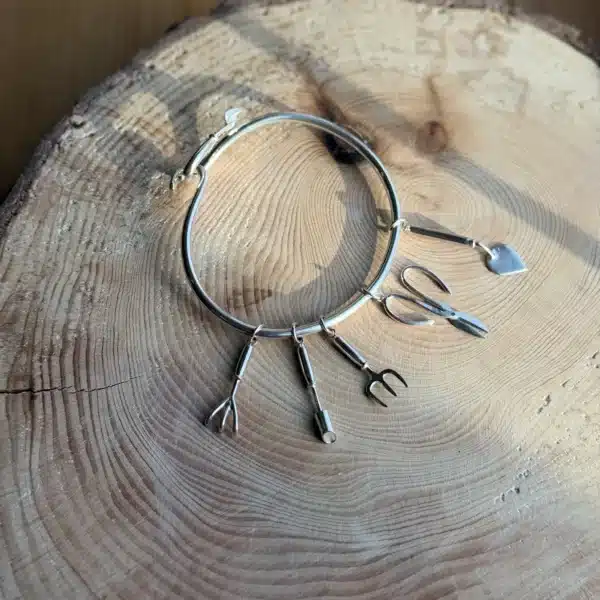 Purple Phoenix Jewellery-Silver trowel bangle with various charms of gardening tools, on a wooden background