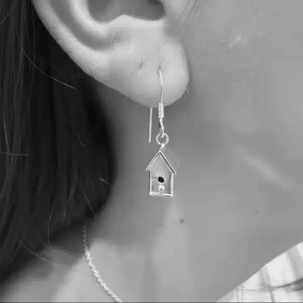 Purple Phoenix Jewellery-Silver miniature birdhouse drop earrings being worn. Black and white image.