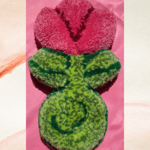 Handmade punch needle pink tulip with textured green leaves and stem, displayed on a pink satin background.