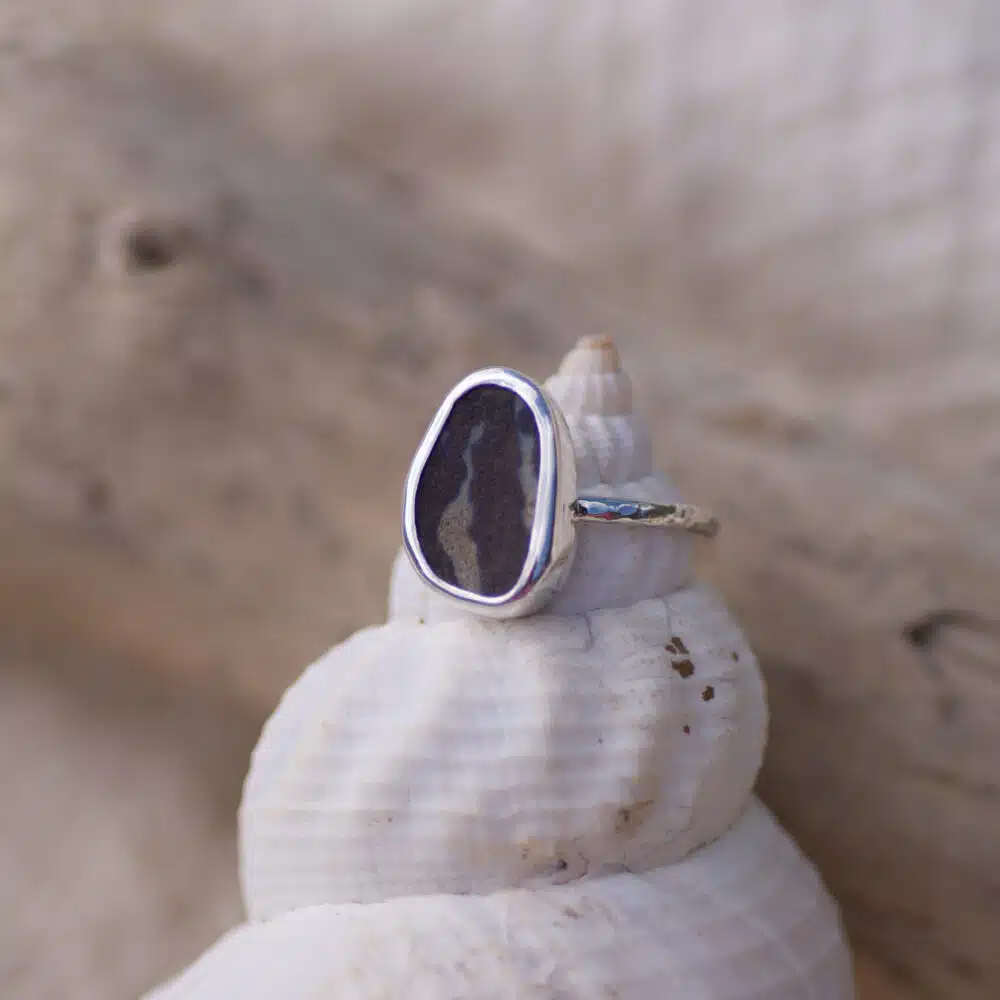 Sea pottery sterling silver ring with a textured band, sitting on the cone of a sea shell with driftwood in the background