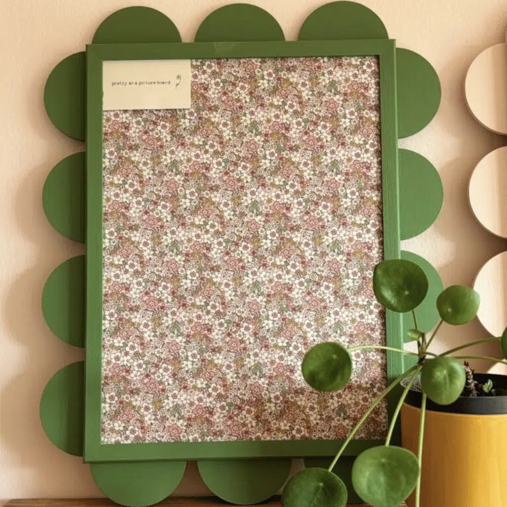 Noticeboard covered in floral fabric in a green scalloped wooden frame