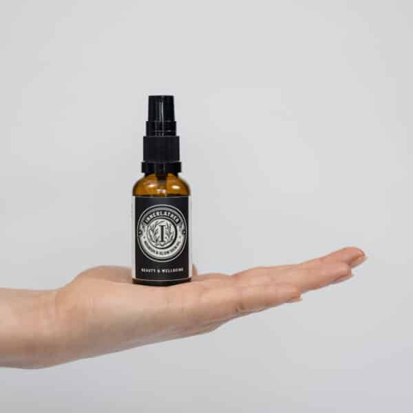 A hand holding a little brown glass bottle of Nourish & Glow Skin Oil