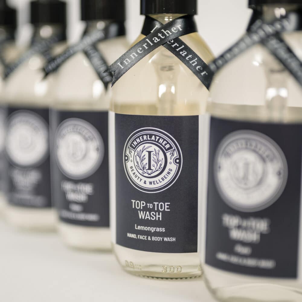 Clear glass bottles of Innerlather Top to Toe Aromatherapy wash.