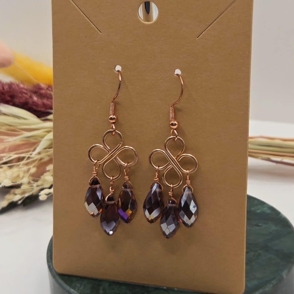 A pair of copper clover/knot-shaped dangle earrings on an earring display card by SunstoneAndFern