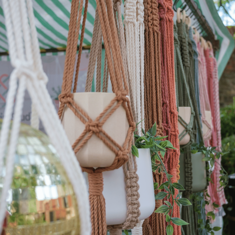 Colourful handmade macramé plant hangers in earthy and pastel tones, displayed with a disco ball and houseplants