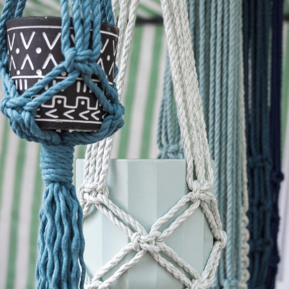 Handmade macramé plant hangers in blue, white and green displayed with potted plants - Sambrini Studio