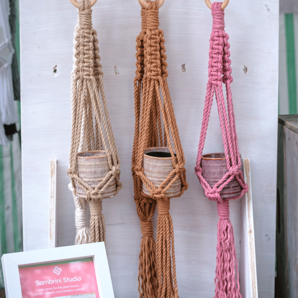 Three small handmade macramé plant hangers in sand, caramel and pink with ceramic plant pots.